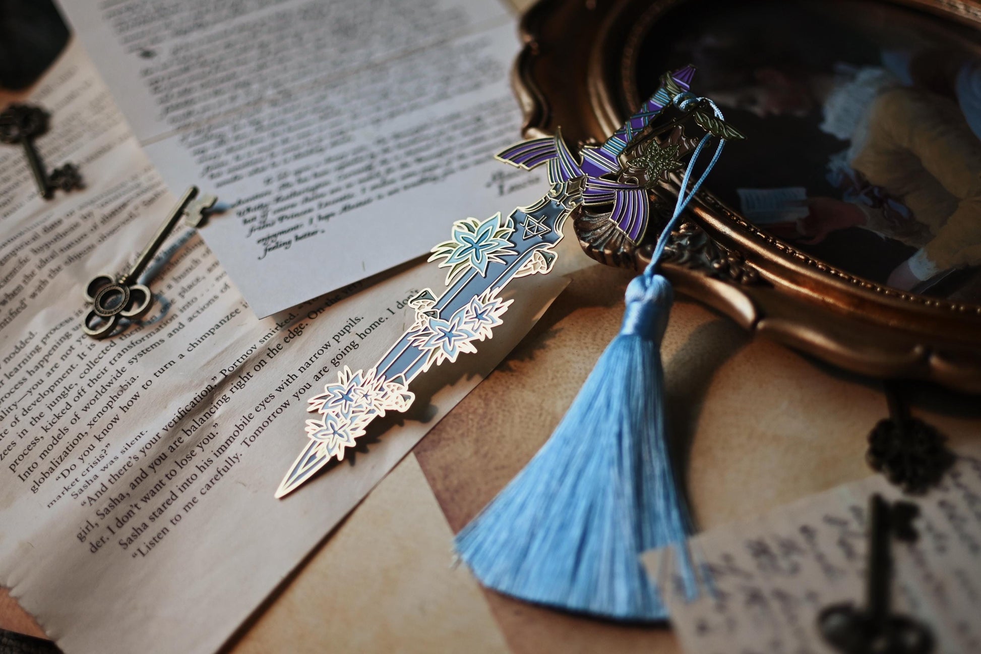 No0neDesigns Link's Master Sword enaml bookmark resting against the end of a painting to lift it against the bacground. The image shows the small details of the pin such as the florals from Hyrule and Korok companion too around the Master Sword.