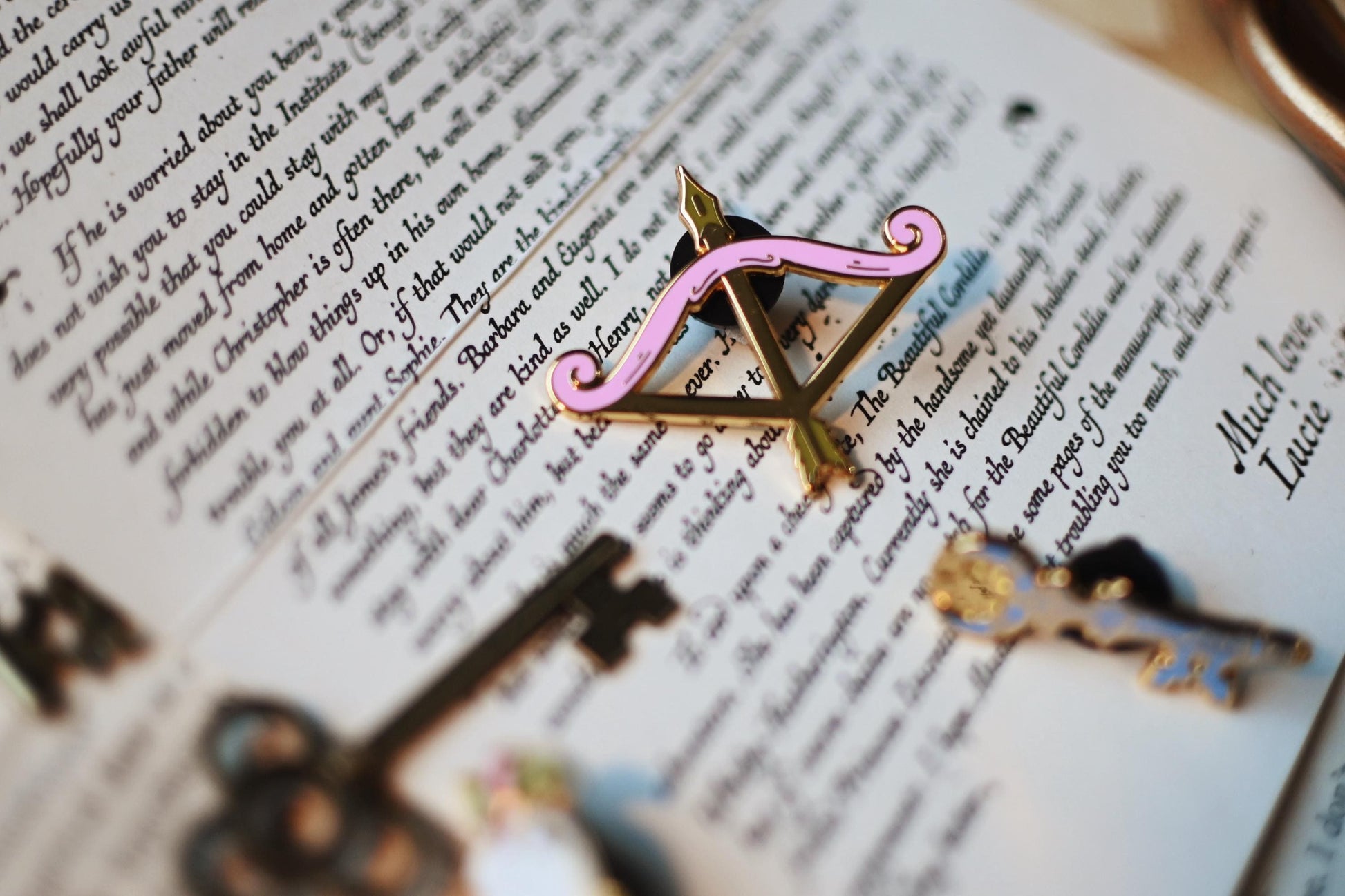 A close up of the once upon a broken heart bow pin featuring gold and pink detailing. 