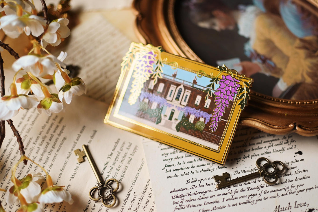 An enamel pin featuring an illustration of Bridgerton House with purple flowers and a yellow frame, placed on a surface with a vintage aesthetic.