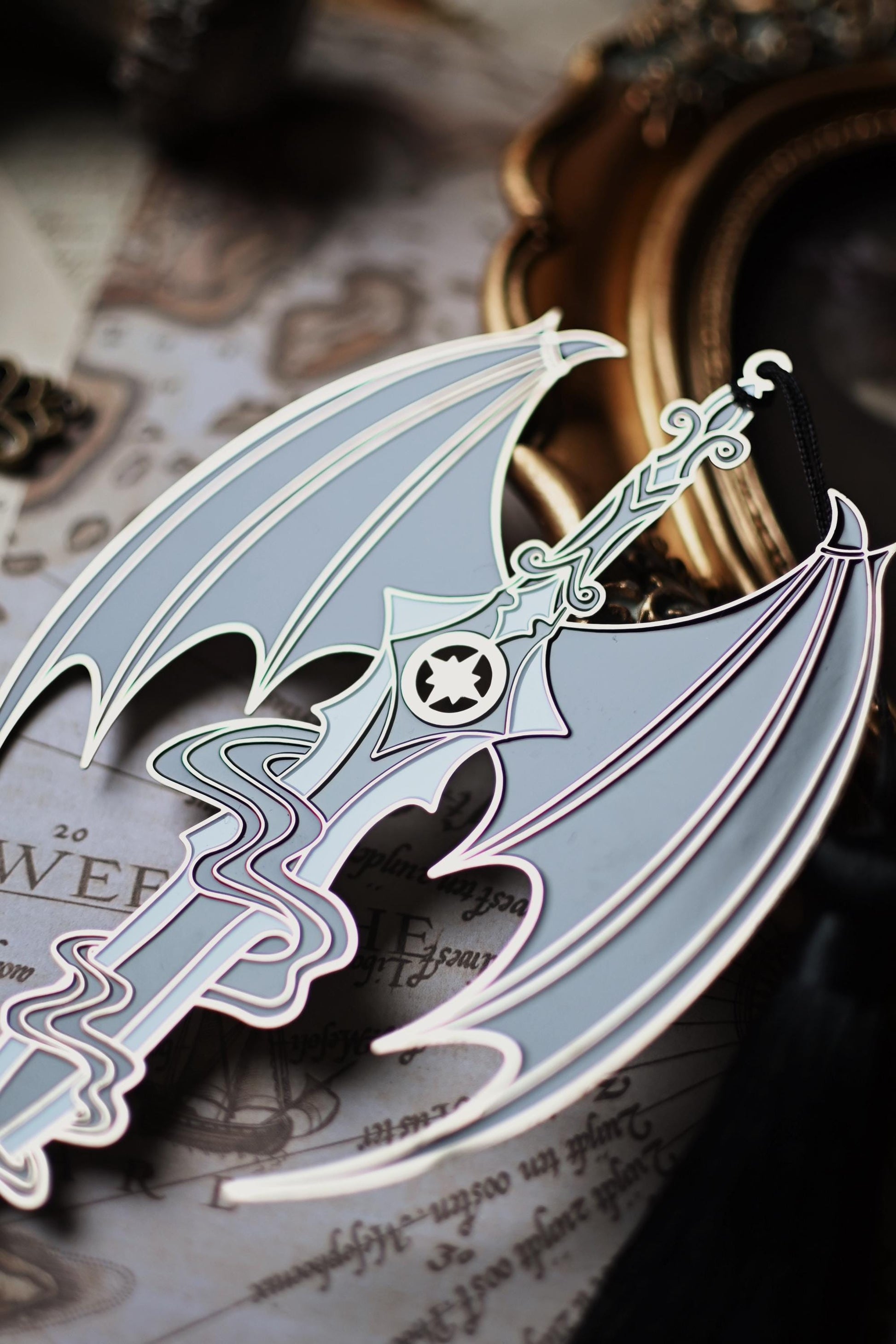 A close up image of the Azriel Shadowsinger Wingspan enamel bookmark focusing on the illyrian wings and hilt of the sword design. 