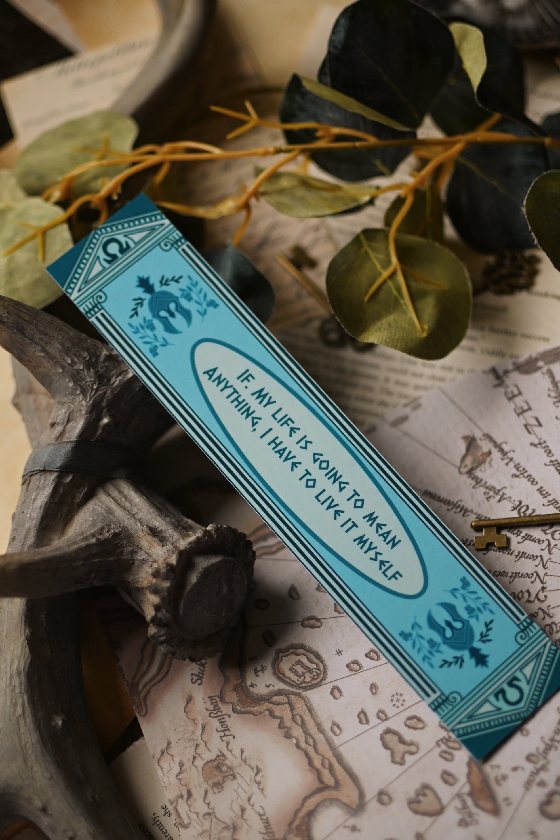 Teal Percy Jackson inspired bookmark with text on a decorative background with greenery and keys. The quote on the bookmark is: If my life is going to mean anything, I have to live it myself. 