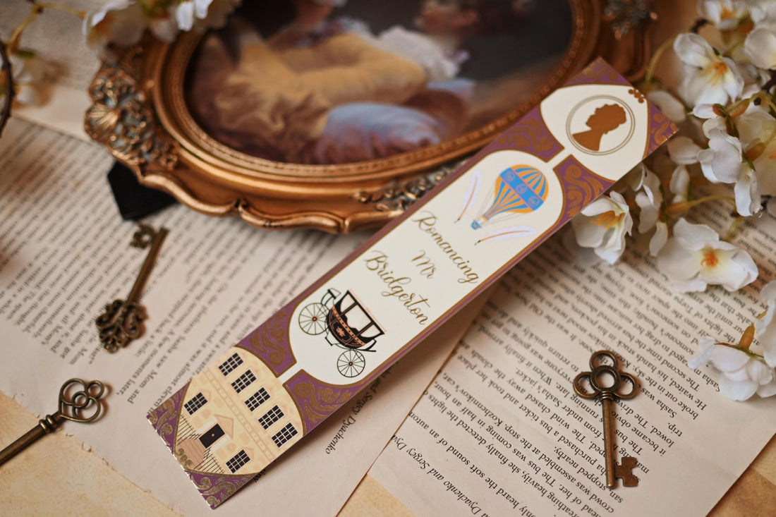 No One Designs Bridgerton-inspired bookmark collection with the three bookmarks fanned out against bookpages and a mirror that raised the bookmarks into the foreground. Each bookmark is inspired by one of Julia Quinn's books and features a gold-foil detailing. Bookmarks inspired by The Duke & I, The Viscount Who Loved Me and Romancing Mr Bridgerton. 