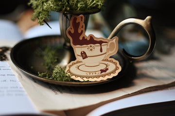 Tea With A Vampire sticker designed by No0neDesigns and inspired by Interview with a vampire propped up against a candle holder to showcase the tea sticker design. 