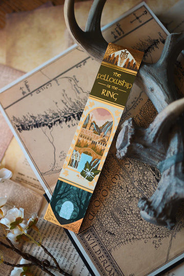 No0neDesigns The Fellowship of the Ring foil bookmark with the sunlight relfecting on the foil. The bookmark is propped up slightly and in the background is a blurred map of middlearth. 