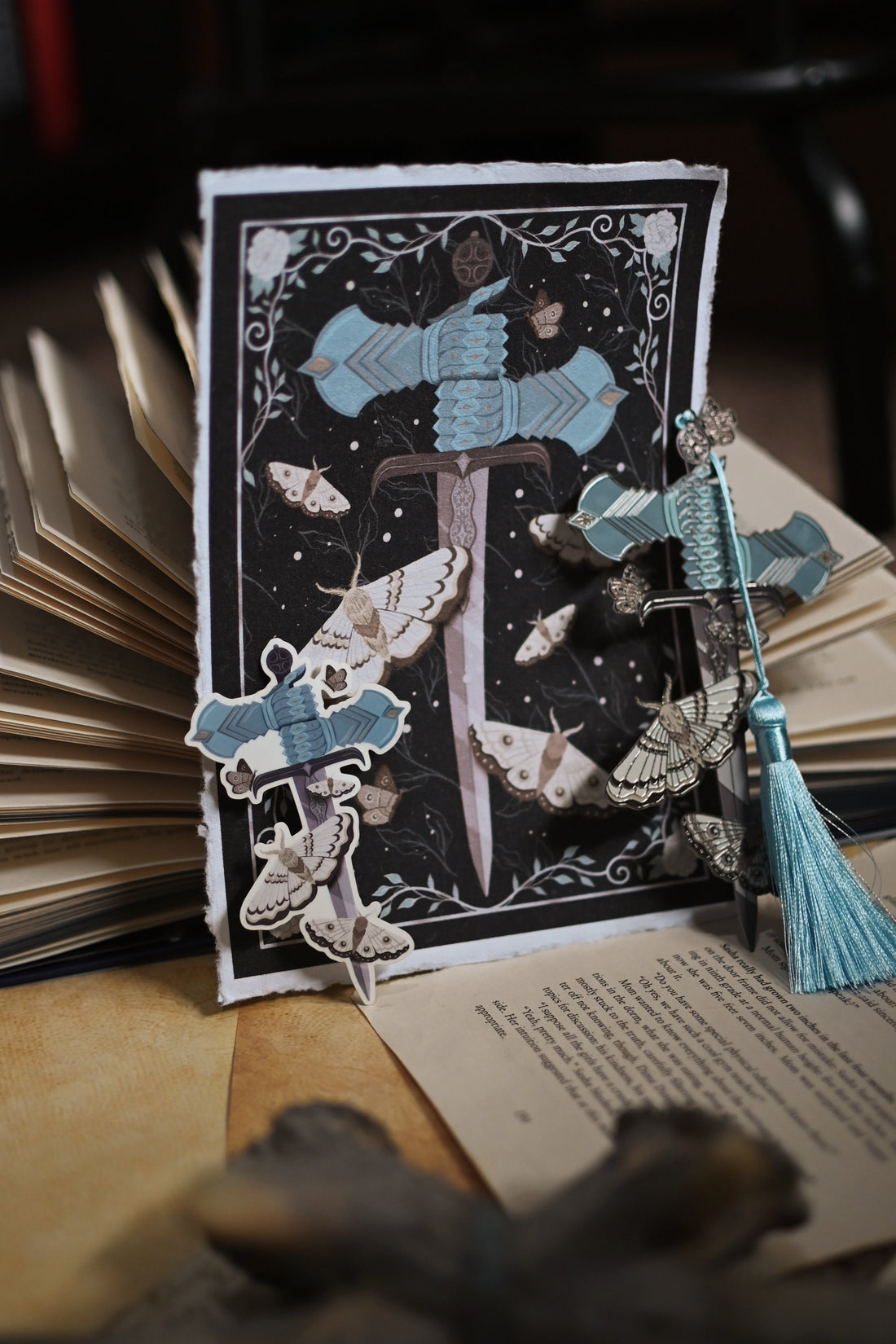 The Knight and the Moth inspired products with the print resting up against an open of the book, sticker and matching enamel bookmark.