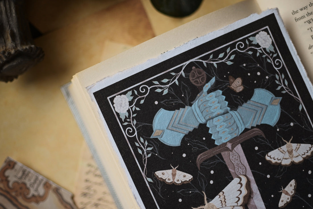 Decorative art print inspired by The Knight and the Moth by Rachel Gillig, the print features with a sword and moth design on a black background with the print resting on an open book page.
