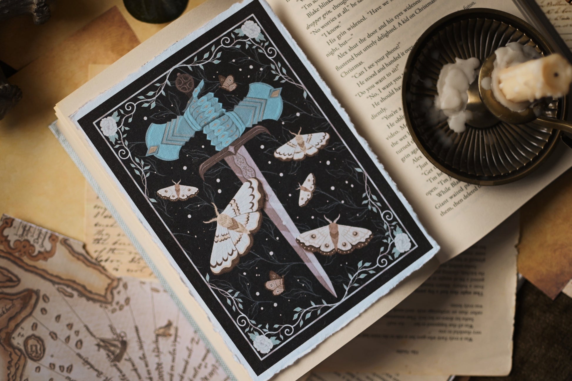 Decorative art print inspired by The Knight and the Moth by Rachel Gillig, the print features with a sword and moth design on a black background with the print resting on an open book page.