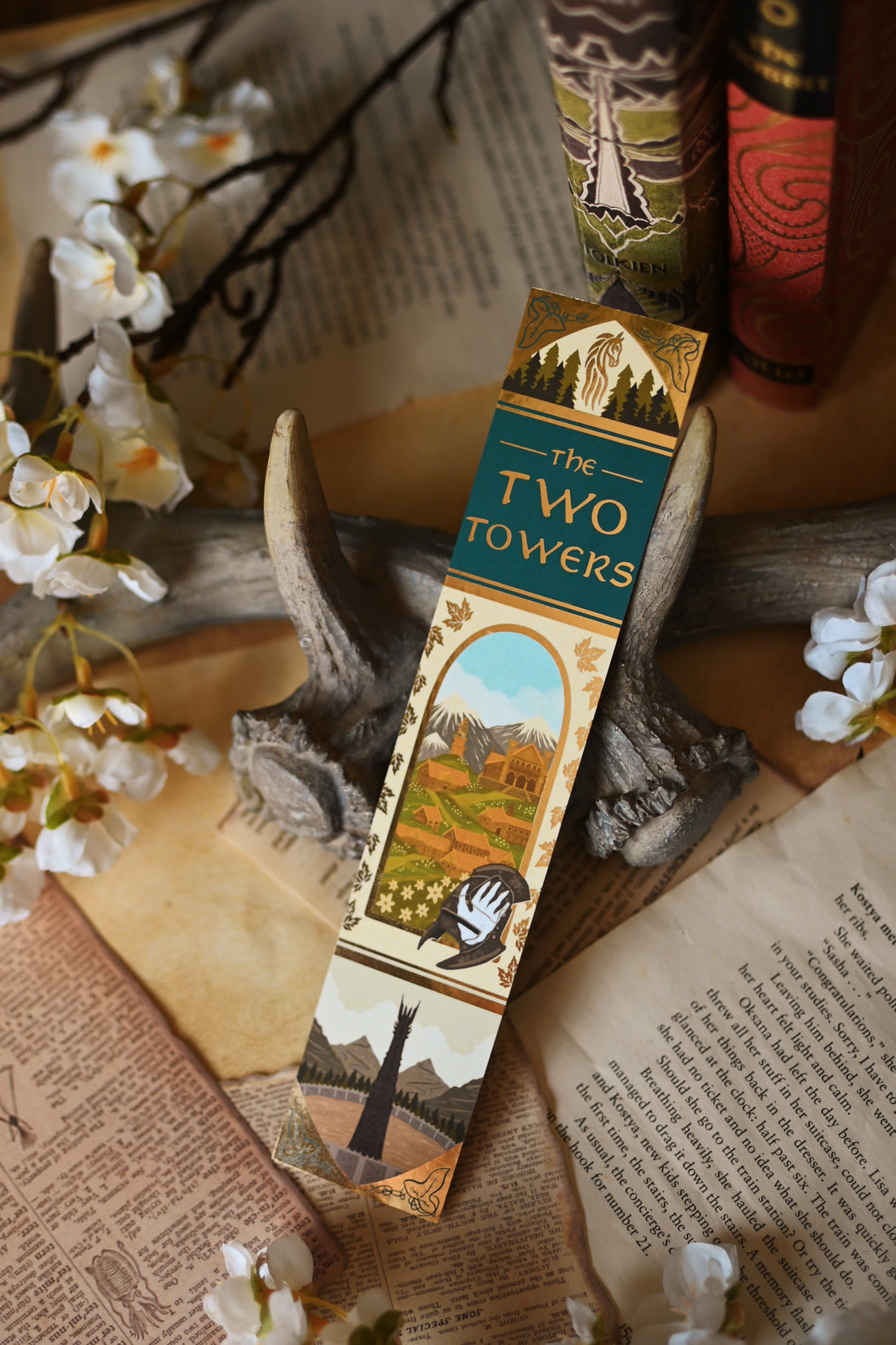 Propped up against a background of stained bookpages and orchid flowers, no0nedesigns foiled bookmark inspired by J.R.R Tolkien's The Two Towers.