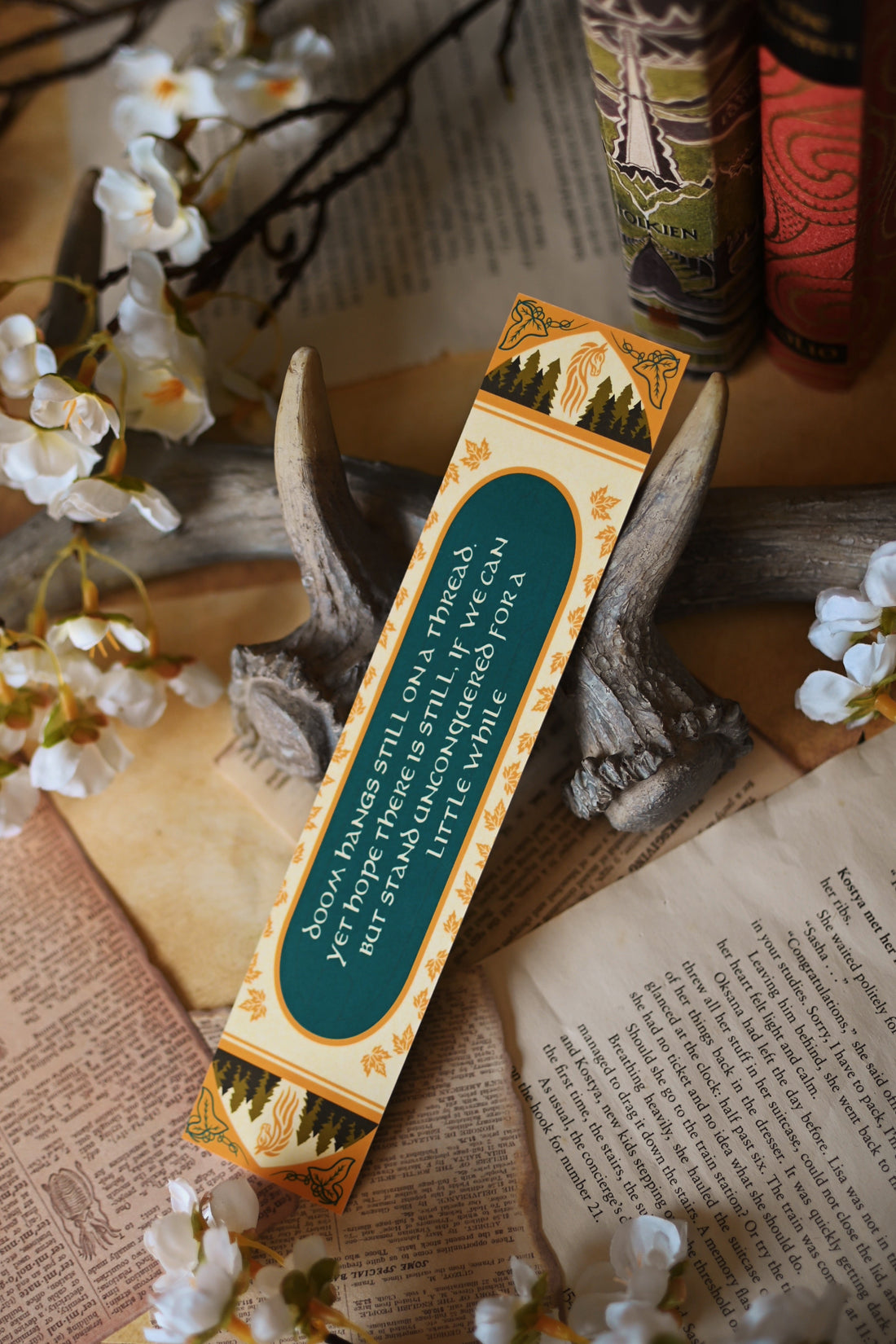 Propped up against a background of stained bookpages and orchid flowers, no0nedesigns foiled bookmark inspired by J.R.R Tolkien's The Two Towers.