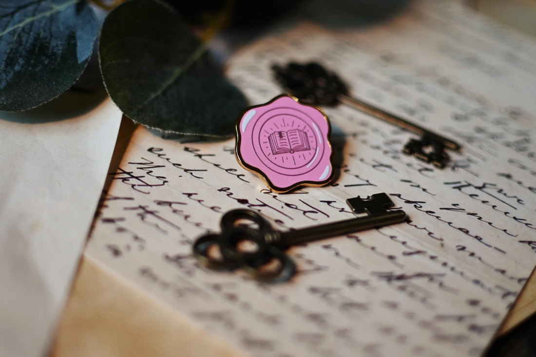 No0neDesigns Bookish Wax Seal enamel pin resting against a background of letters that were hand written and antique keys.
